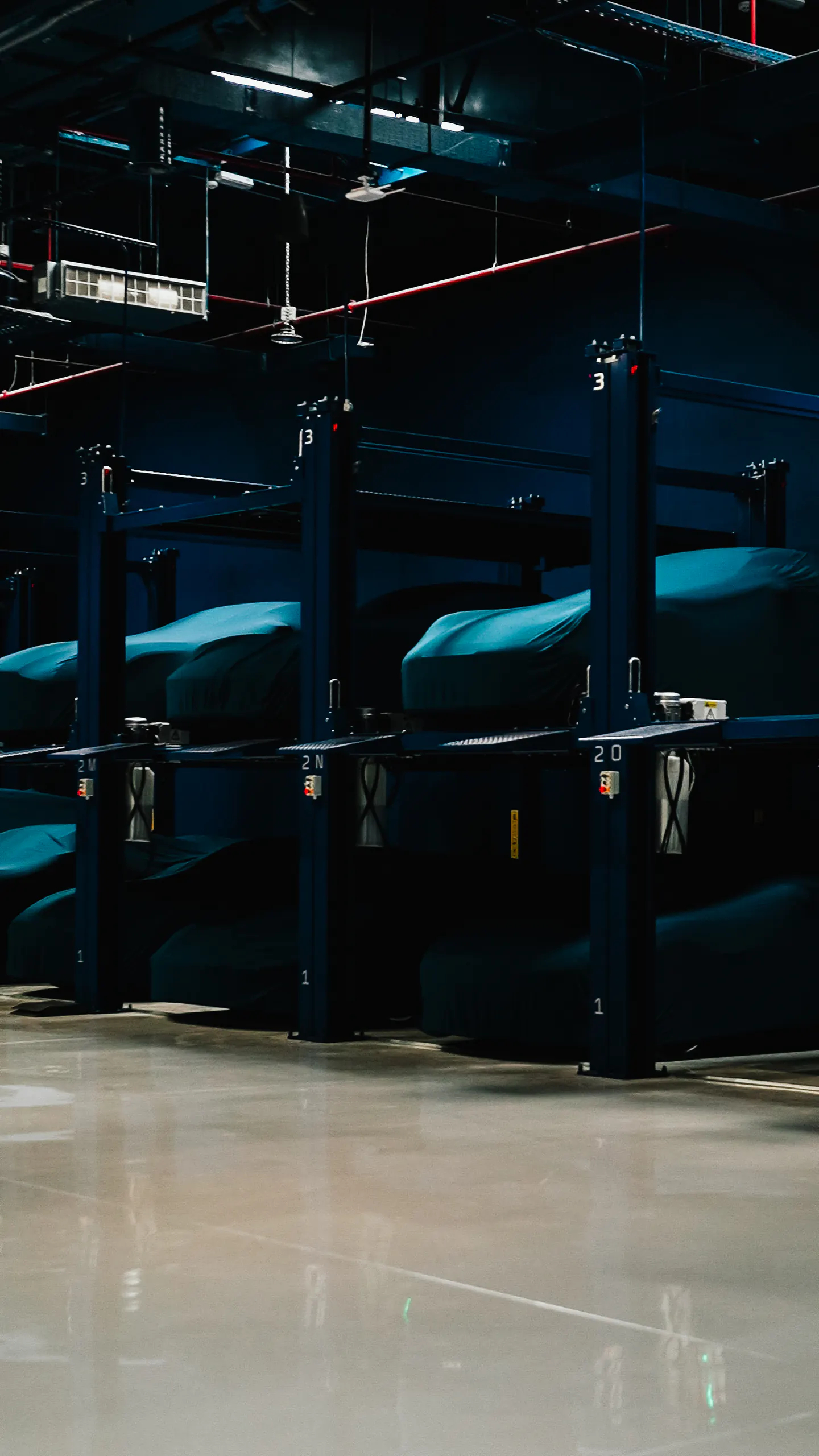 Covered cars resting in individual numbered bays on two-tier storage lifts inside the Hangar